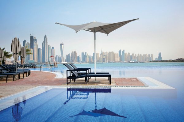 Voilá Umbrella - Taupe providing shade to beach chairs next to a large pool