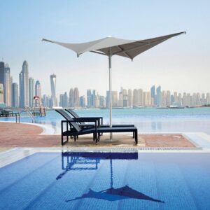 Voilá Umbrella - Taupe providing shade to beach chairs next to a large pool