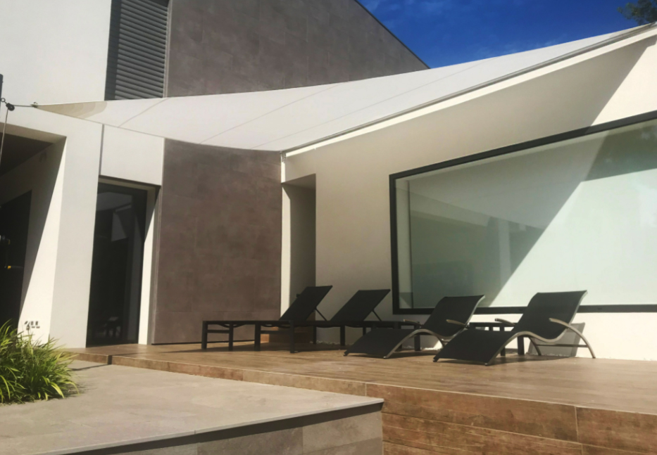 Velart Sail Shade providing shade to 4 outdoor lounge chairs beside a building