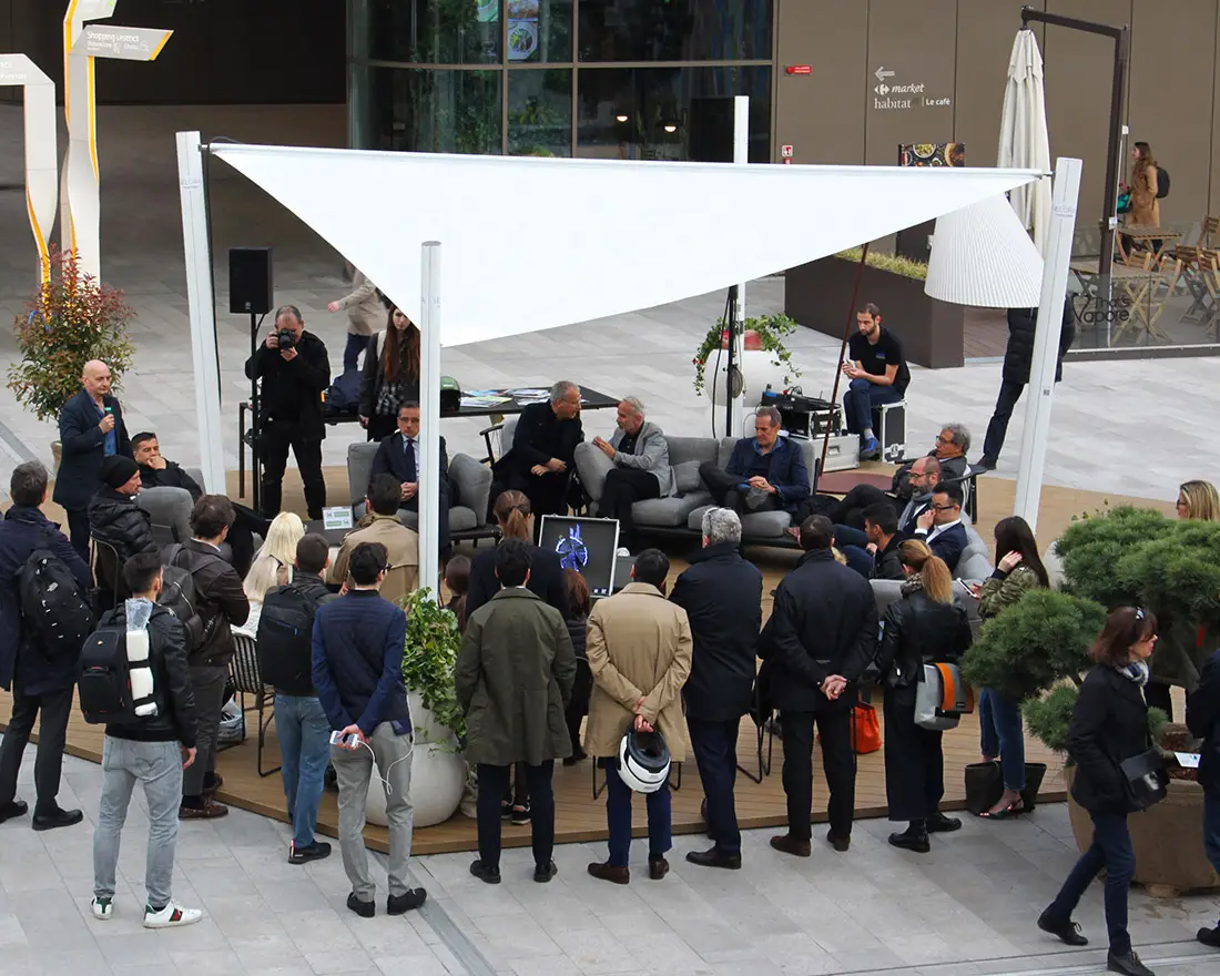 People working and gathering at a seating area under a Velora Sail Shade